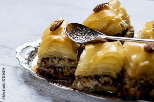 Closeup on a baklava on a silver tray with an ornamental spoon o a white wooden background photo