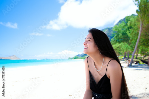 Biracial teen girl sitting at Hawaiian beach, side profile, smiling