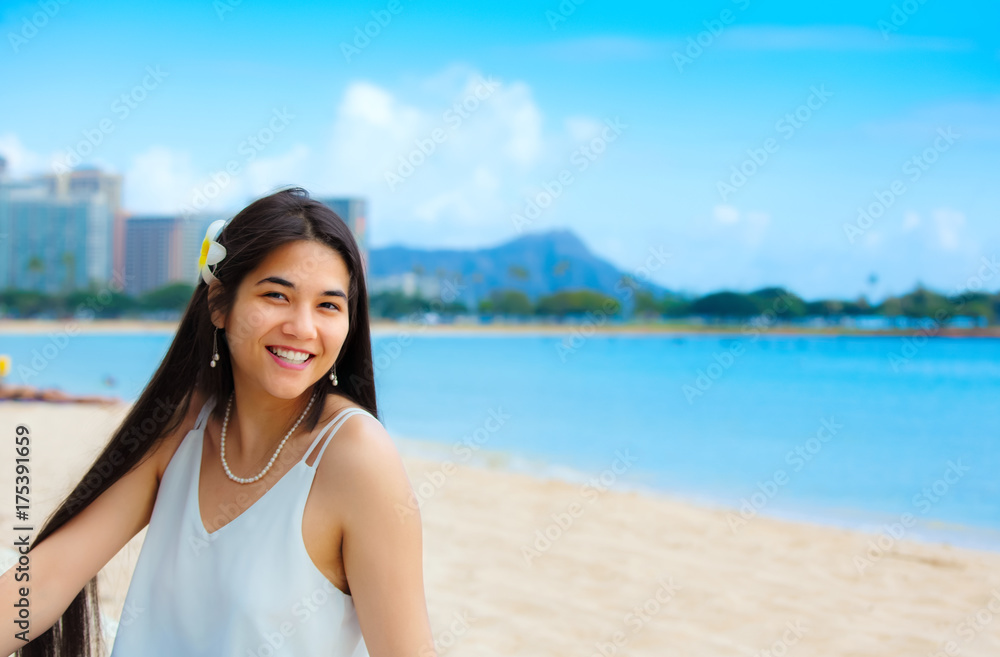 Teen girl sitting on Hawaiian beach, Diamond Head in background