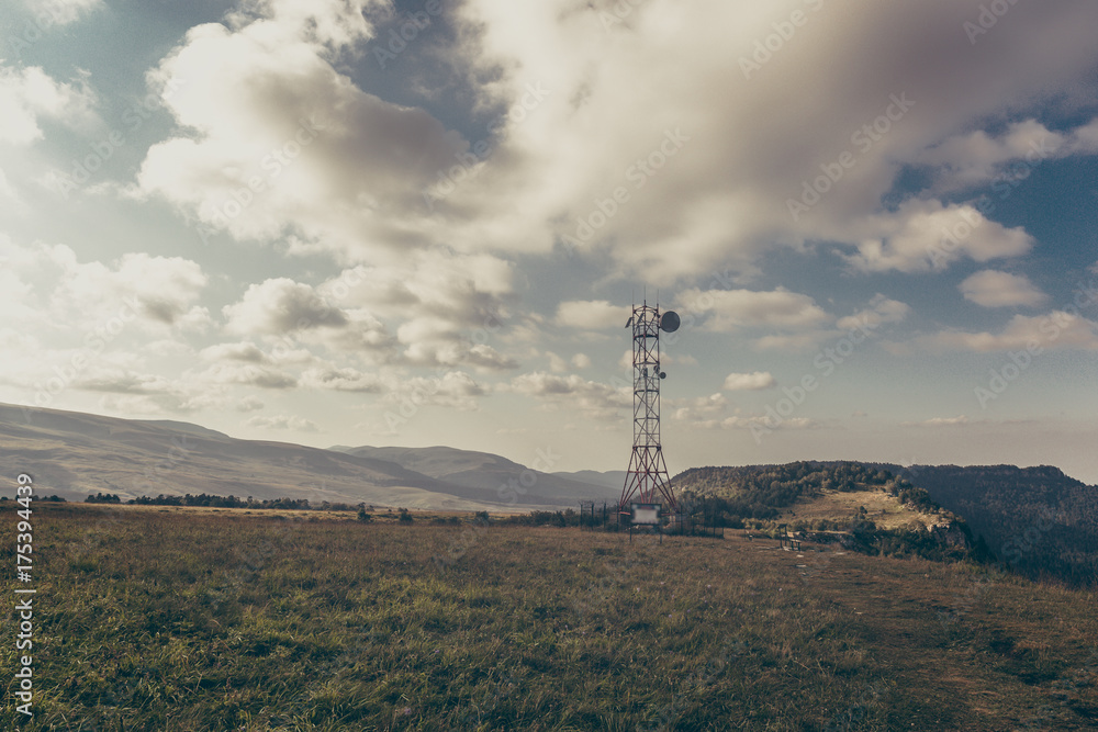 Communication tower antenna on mountain plateau against sky background in alpine terrain