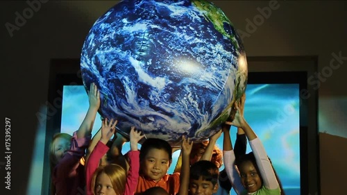 Tilt down, group of kids lift up globe in front of aquatic background