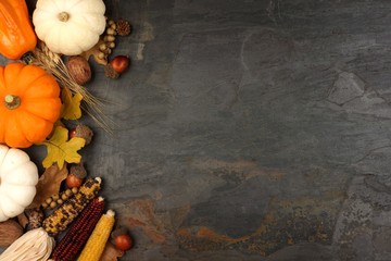 Autumn harvest side border with pumpkins, leaves and nuts over a slate stone background