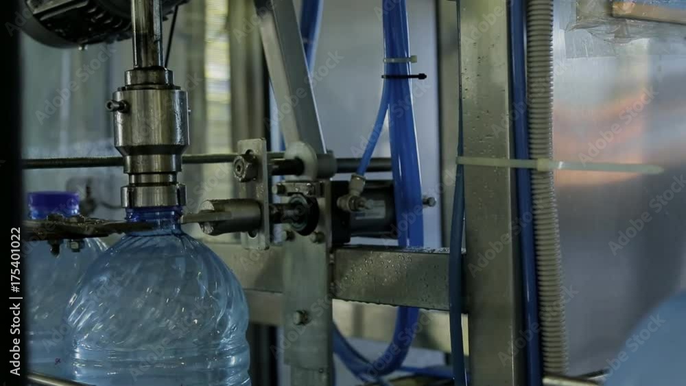 Closing plastic bottles with water on conveyor belt in modern company indoor. Transparent containers filled with clean drinking aqua move along automatic line and at the same time, with help of metal