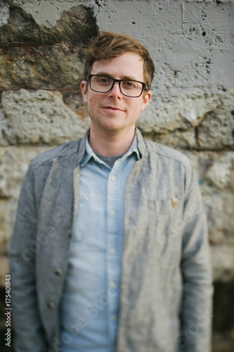 Hipster guy near old abandoned building with thick framed glasses and denim button up shirt photo