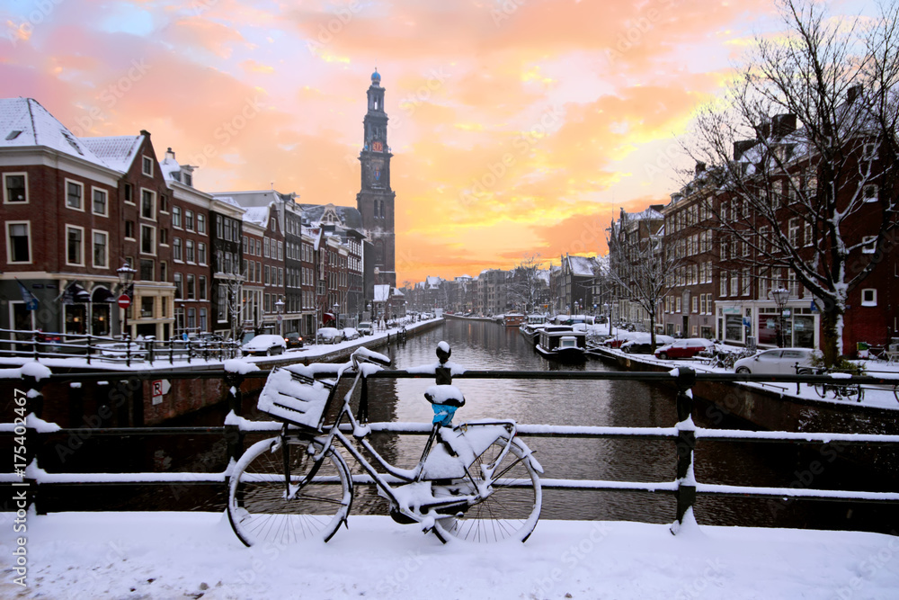 Naklejka premium Amsterdam pokryty śniegiem z Westerkerk zimą w Holandii o zachodzie słońca
