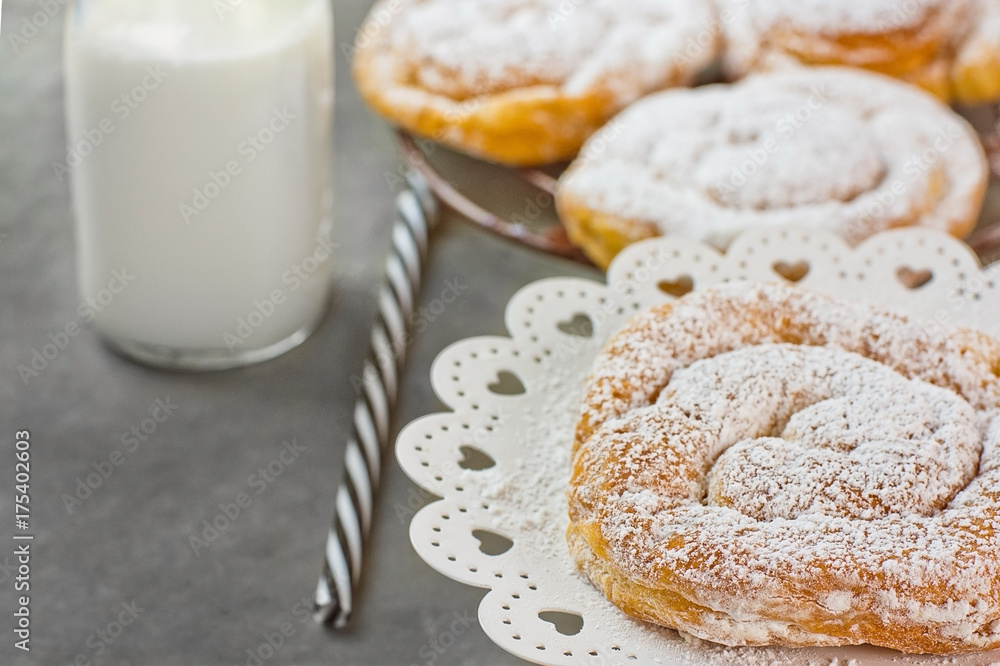 Swirl Danish Pastry Powdered on Cooling Rack and Cake Stand. Bottle of Milk Striped Straw. Dark Tabletop. Swirl Danish Pastry Powdered on Cooling Rack and Cake Stand. Bottle of Milk Striped Straw. Dark Tabletop.