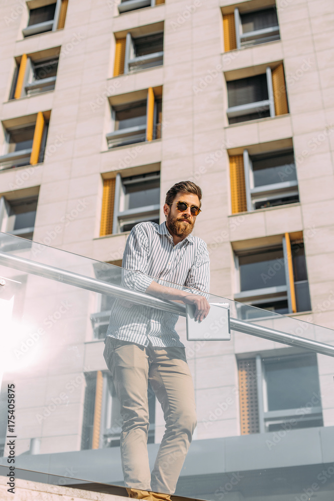 Young Caucasian businessman using a digital tablet in front of a corporate building. Young Caucasian businessman using a digital tablet in front of a corporate building.