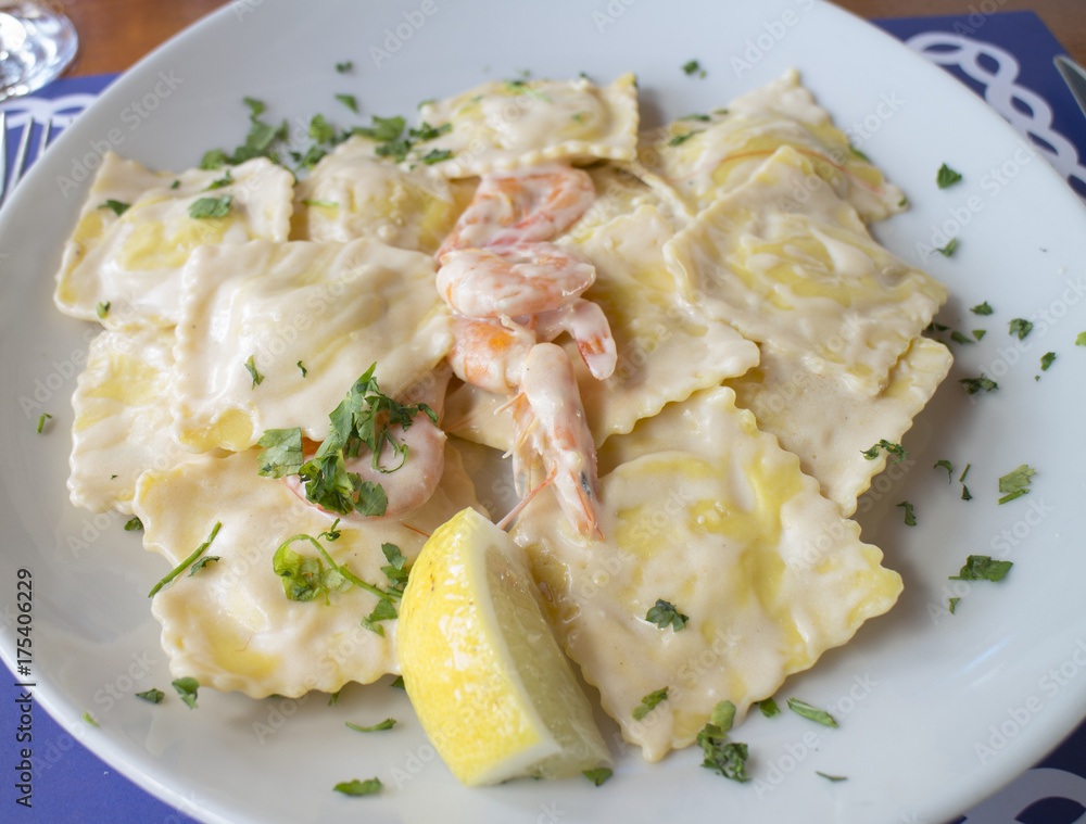 Ravioli ai frutti di mare / Closeup of a typical dish of Italian seafood cuisine homemade with padded pasta, white sauce and little shrimps Ravioli ai frutti di mare / Closeup of a typical dish of Italian seafood cuisine homemade with padded pasta, white sauce and little shrimps