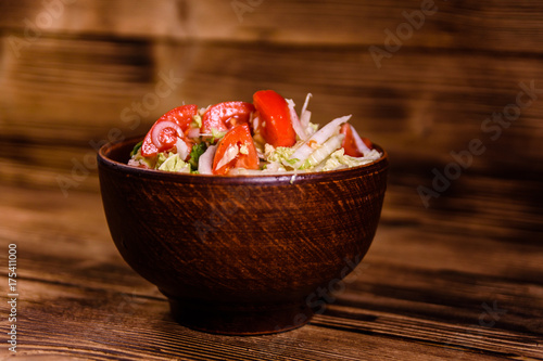 Dietary salad with the chinese cabbage and tomatoes in ceramic bowl on a wooden table