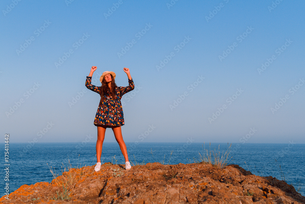 Beautiful girl in a dress and with a hat in the mountains against the sea