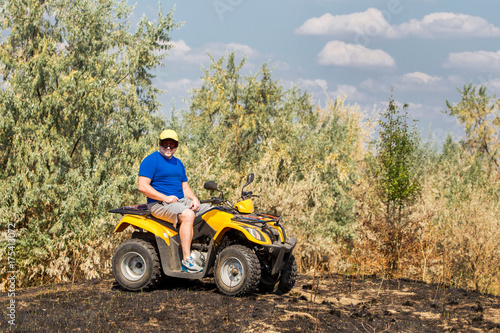 Caucasian man in sport protective goggles riding an ATV quad bike over rough terrain with meadows of dry autumn grass. Adventure activity concept