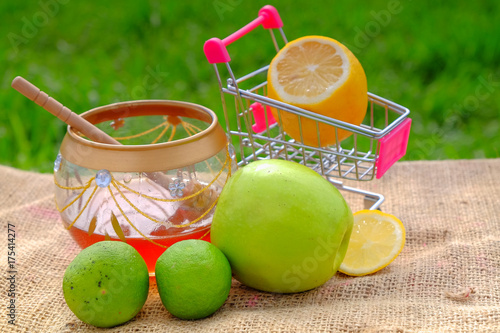 Sweet honey in the jar, shopping cart, lime  and green apple with blurred background. Conceptual image of buying vegetables and healthy eating. photo