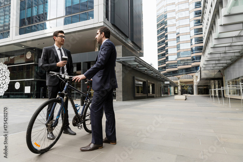 Two young businessmen with a bike in city centre © Sergey Nivens