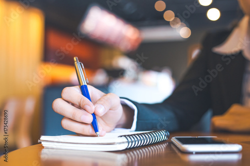 business woman hand using mobile phone and writing on notepad with a pen in office.