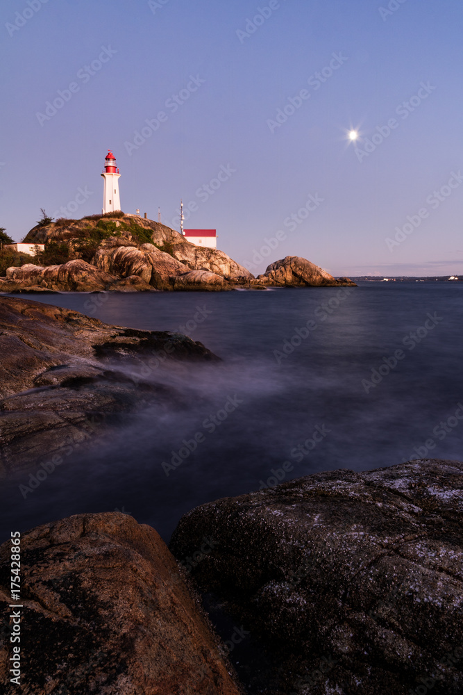 Full moon rising behind a lighthouse. rocky shore line on the pacific northwest coast of Canad