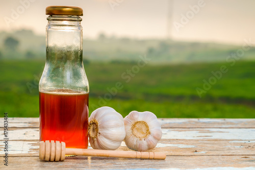 Fresh organic honey in glass jar , garlic and honey stick on old wooden with blurred background , healthy nutrition, strengthening immunity and treatment of flu photo