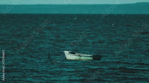 Wooden shallop rocking on waves in middle of lake, segulls flying over, sunny summer windy day photo