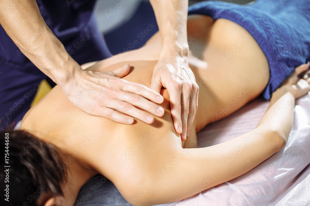 Closeup of male hands of massage therapist massaging woman's back