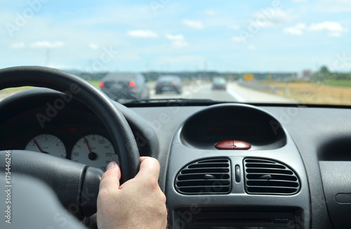 Man driving a car with a dirty front glass after a long drive on a highway with other vehicles blurred in front of him