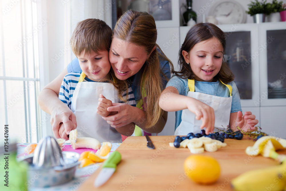 Happy young kids with their mother in the kitchen - preparing a healthy fruit snack Happy young kids with their mother in the kitchen - preparing a healthy fruit snack