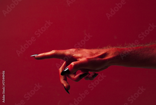 Halloween red devil monster hand with black fingernails against a red background