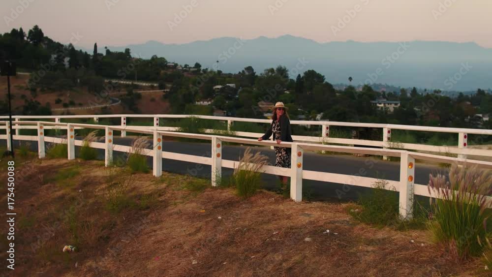 Cute woman looking at sunset summer and fall dress and hat walking up on a mountain aerial shot Los Angeles California Cute woman looking at sunset summer and fall dress and hat walking up on a mountain aerial shot Los Angeles California