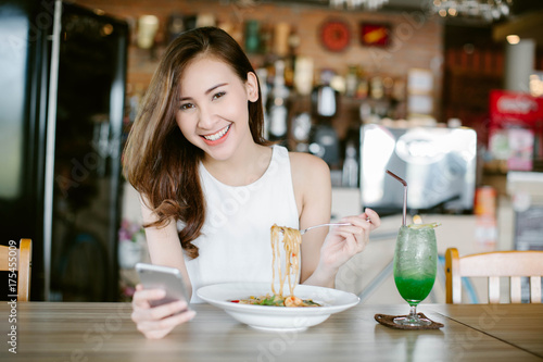 Young Asia woman eating food at restaurant and using on smart phone