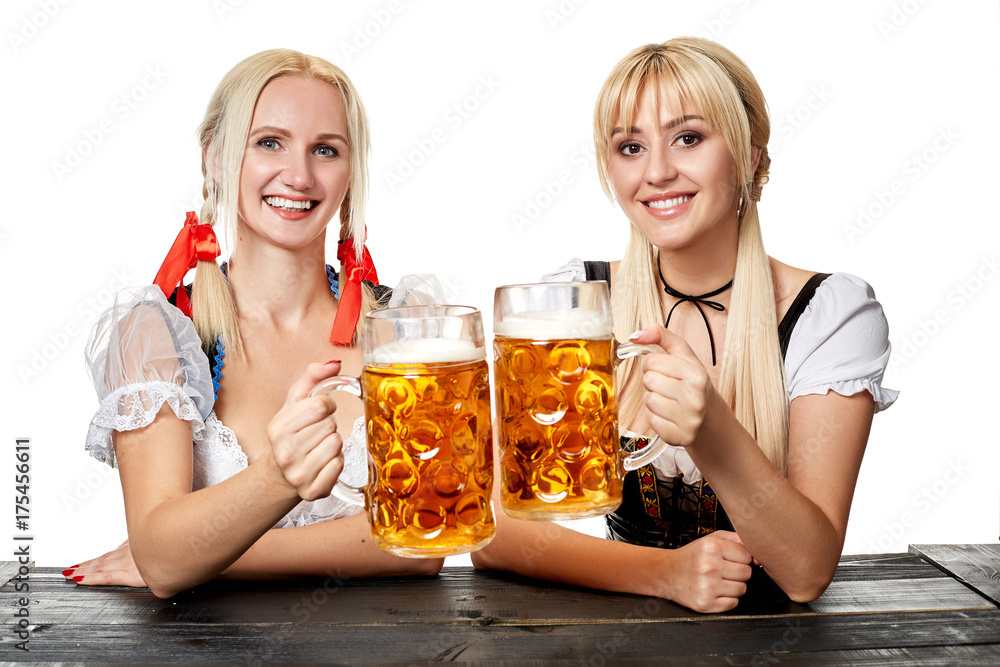 Two beautiful women holding a glass of beer while sitting at a wooden table on a white background in the studio Two beautiful women holding a glass of beer while sitting at a wooden table on a white background in the studio