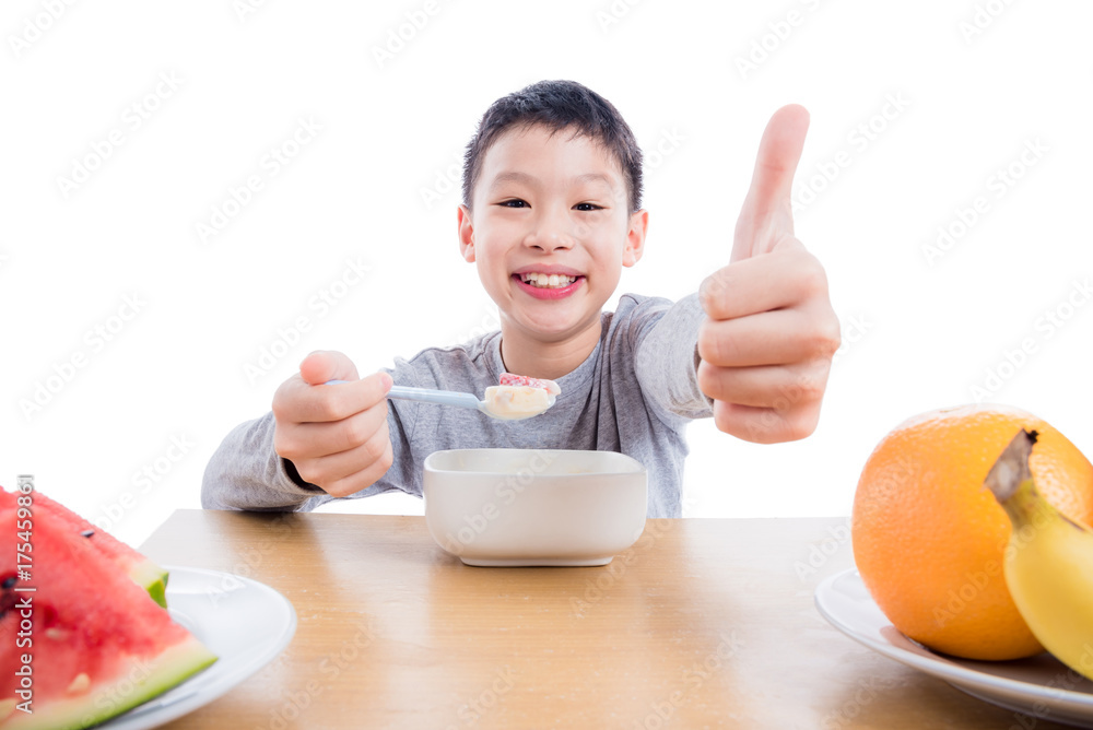 Young asian boy eating cereal with yogurt for breakfast over white background Young asian boy eating cereal with yogurt for breakfast over white background