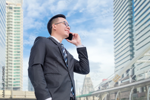 Bild auf Leinwand Young asian businessman wearing black suit talking via smart phone with modern b