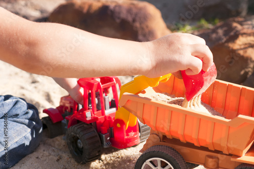 A child plays in the sand with big toy cars, an excavator, a truck