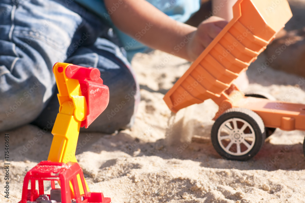 A child plays in the sand with big toy cars, an excavator, a truck A child plays in the sand with big toy cars, an excavator, a truck