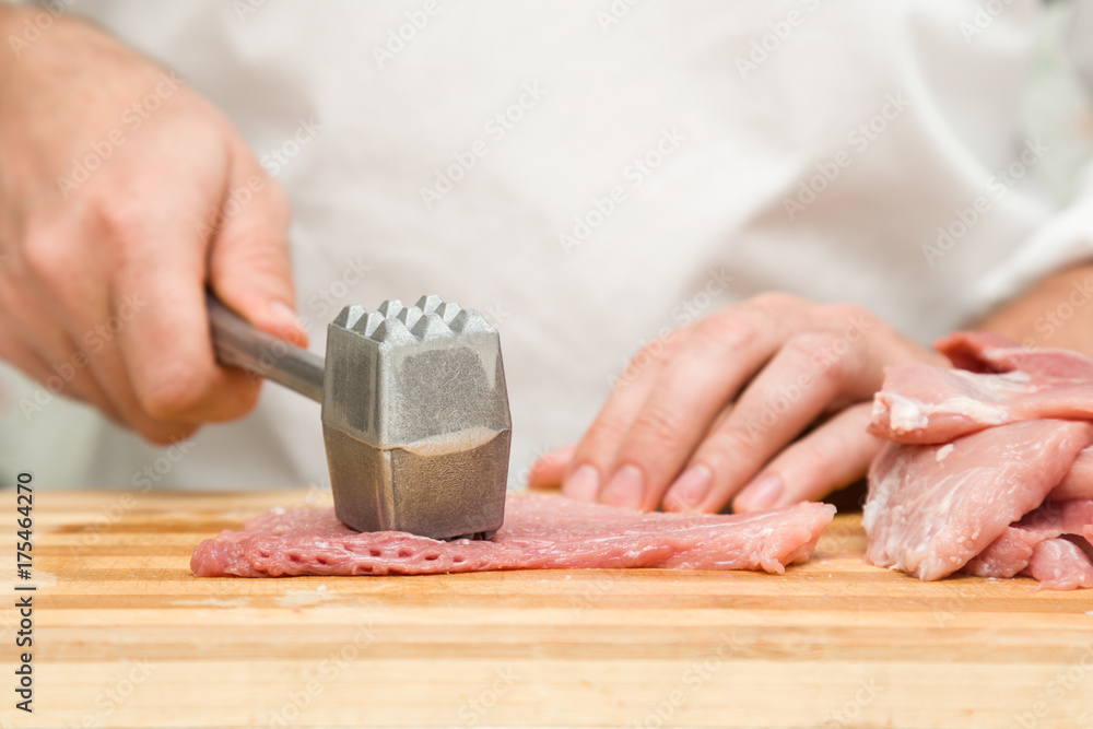 Chef's hands with a hammer beating a meat on the wooden board in the kitchen. Preparation for cooking. Food concept. Chef's hands with a hammer beating a meat on the wooden board in the kitchen. Preparation for cooking. Food concept.