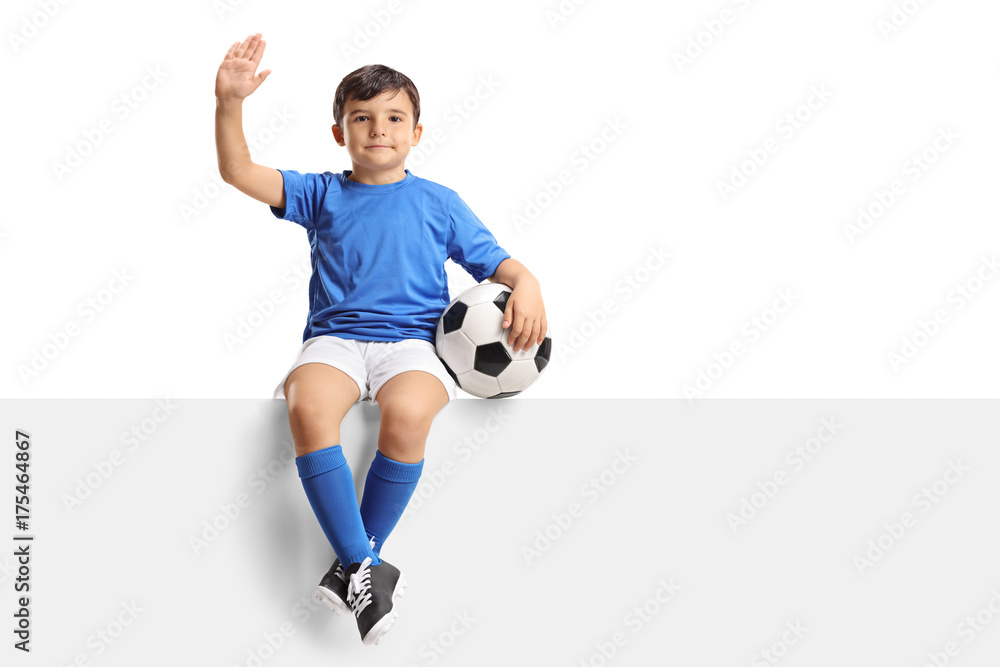 Small boy with a football sitting on a panel and waving
