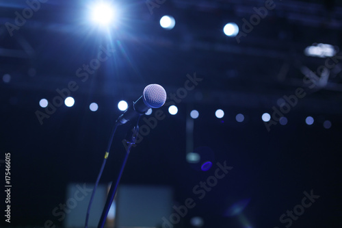 Close up of microphone in concert hall or conference room with cold lights in background.