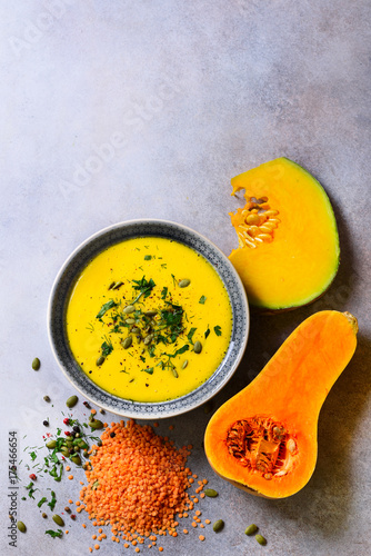 Vegetable and lentils creamy soup, cut pumpkin, seeds, parsley on light grey background. Top view, copy space