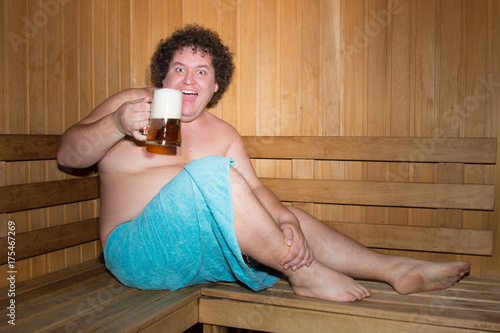 Funny fat man in a sauna with a beer.  photo