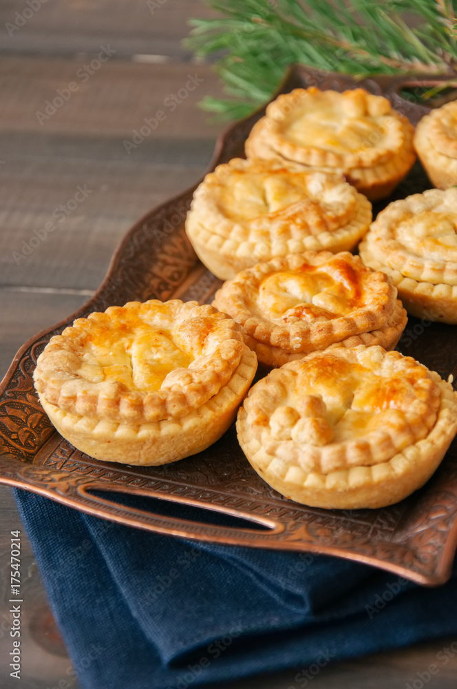 Mini meat pies from flaky dough on a vintage tray over wooden background.