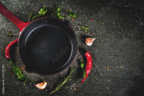 Cooking background with skillet and spices - hot pepper, garlic, basil, rosemary, salt, black stone table, top view copy space