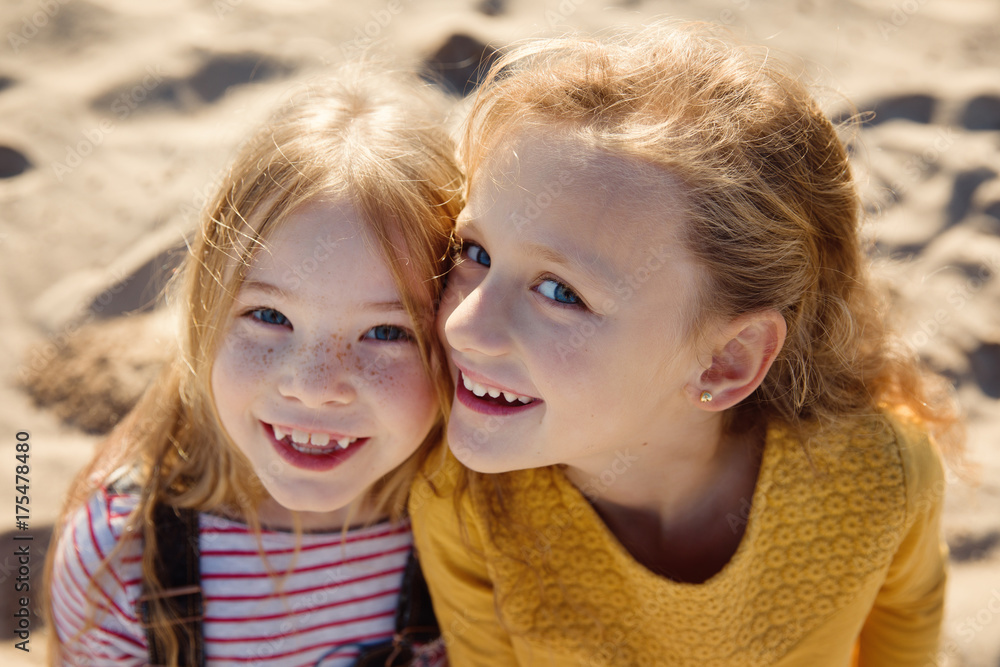Two happy little girls cheek to cheek on a sandy beach Two happy little girls cheek to cheek on a sandy beach