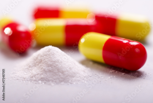 white powder drugs with yellow red capsules on white background photo