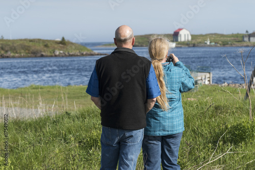 Leinwand Poster Rear view of couple taking picture with camera at riverbank, Cape Breton Island,
