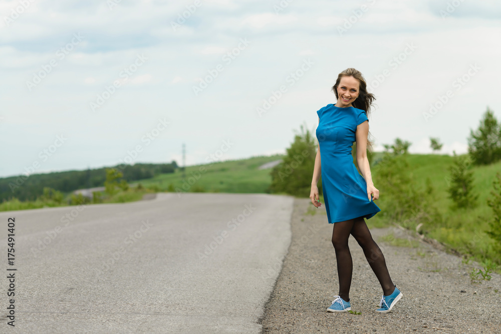 Beautiful woman in a blue dress posing on a road over landscape