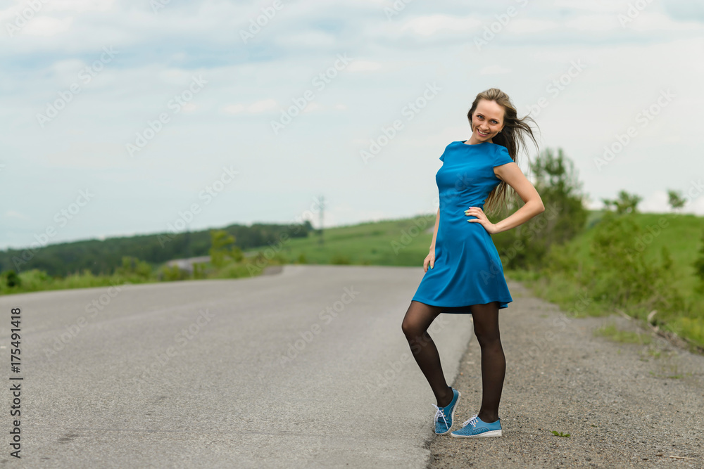 Beautiful woman in a blue dress posing on a road over landscape Beautiful woman in a blue dress posing on a road over landscape