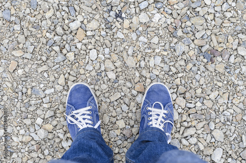 Texture of stones with sharp edges and legs in jeans and blue sneakers