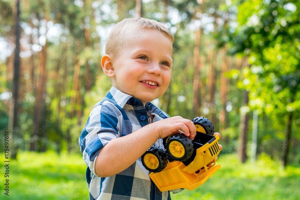 Little boy is playing with a yellow toy car in the park