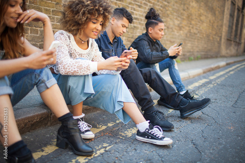 Four friends sitting in street, looking at smartphones