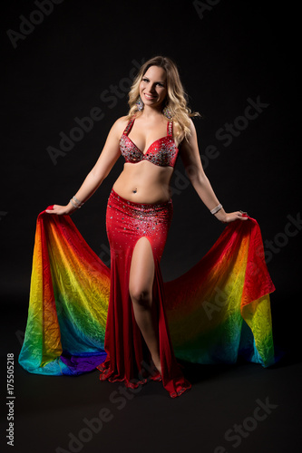 Beautiful belly dancer holding veil and performing belly dance on black background.