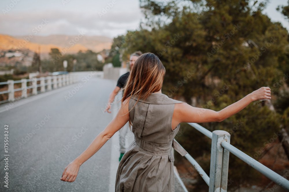 Woman in her back dancing in front of a man on a bridge in a rural landscape.