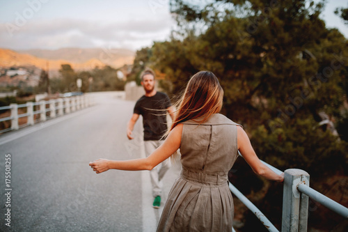 Woman in her back dancing in front of a man on a bridge in a rural landscape.
